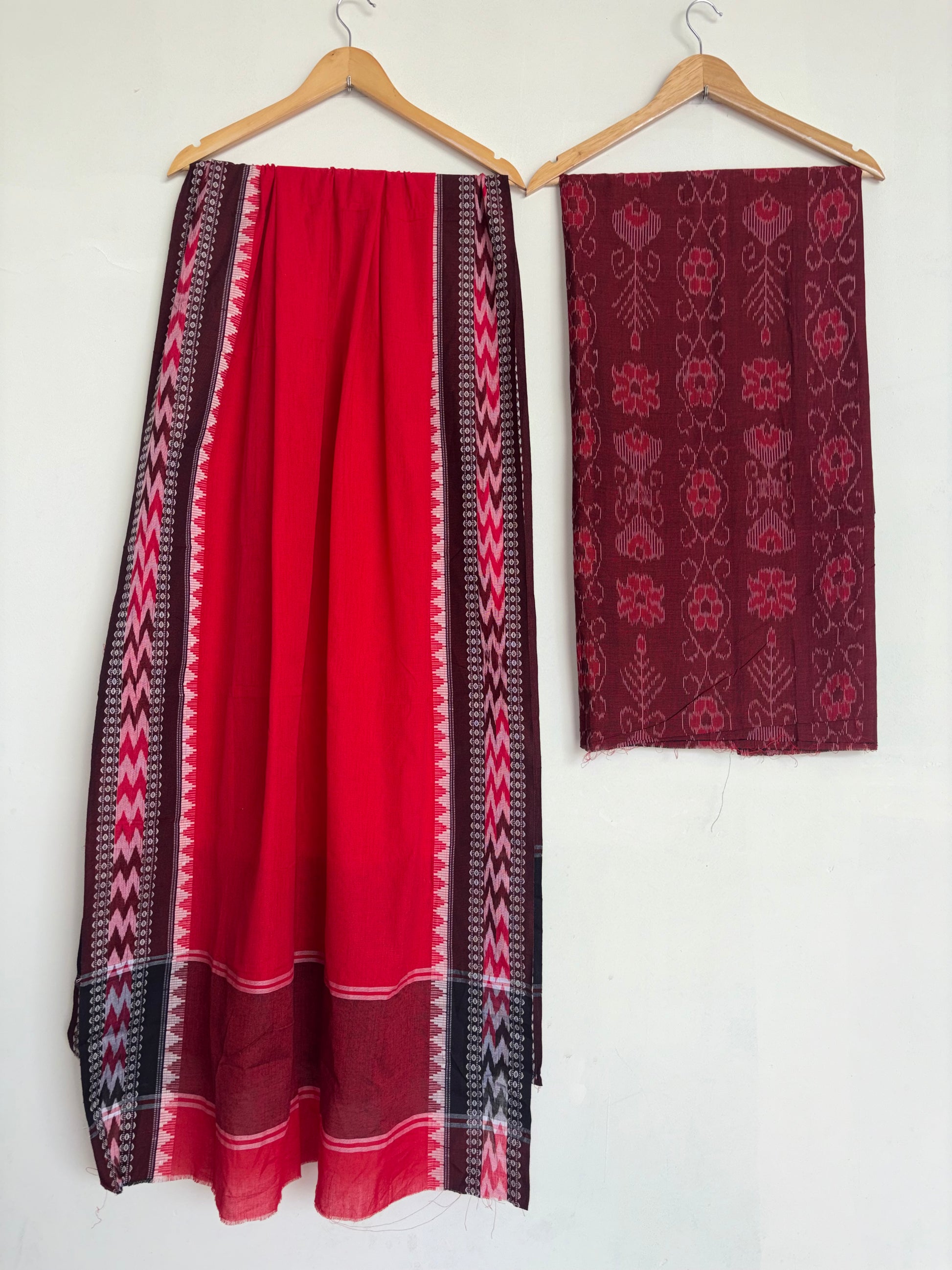 A red and black patterned skirt hanging on a wooden hanger next to a matching dark red patterned fabric piece on a white wall.