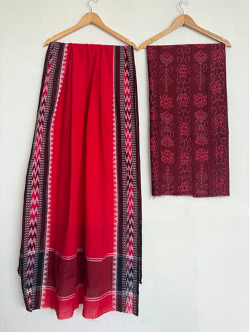 A red and black patterned skirt hanging on a wooden hanger next to a matching dark red patterned fabric piece on a white wall.